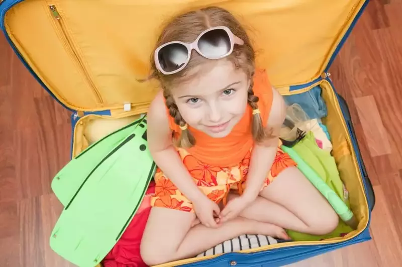 child sitting on packed suitcase